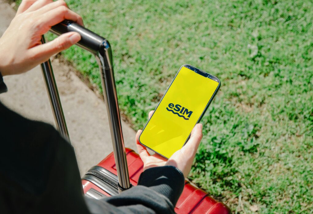 A person holds a smartphone showing an eSIM app while standing with luggage outdoors in Los Angeles.