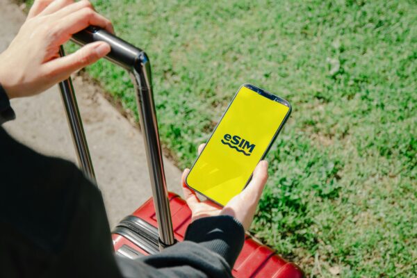 A person holds a smartphone showing an eSIM app while standing with luggage outdoors in Los Angeles.