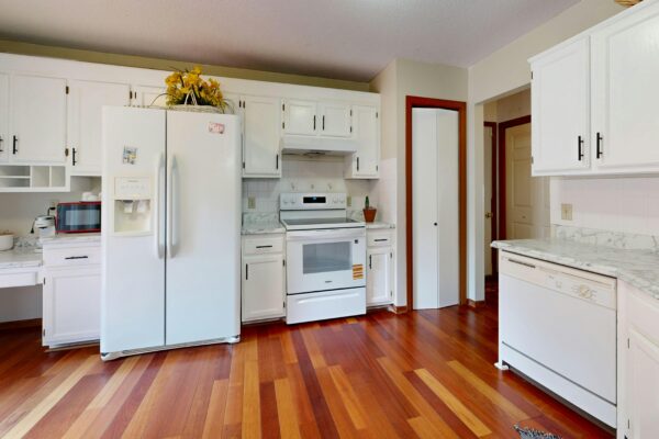 Bright kitchen featuring white cabinets and appliances with hardwood floors.