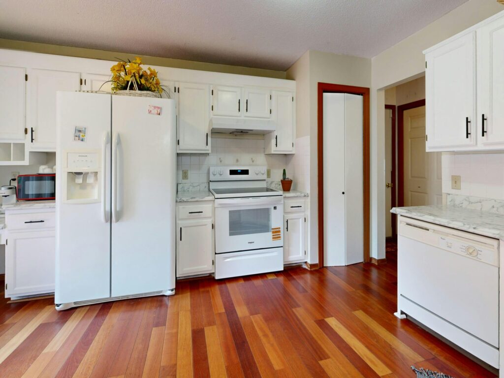 Bright kitchen featuring white cabinets and appliances with hardwood floors.